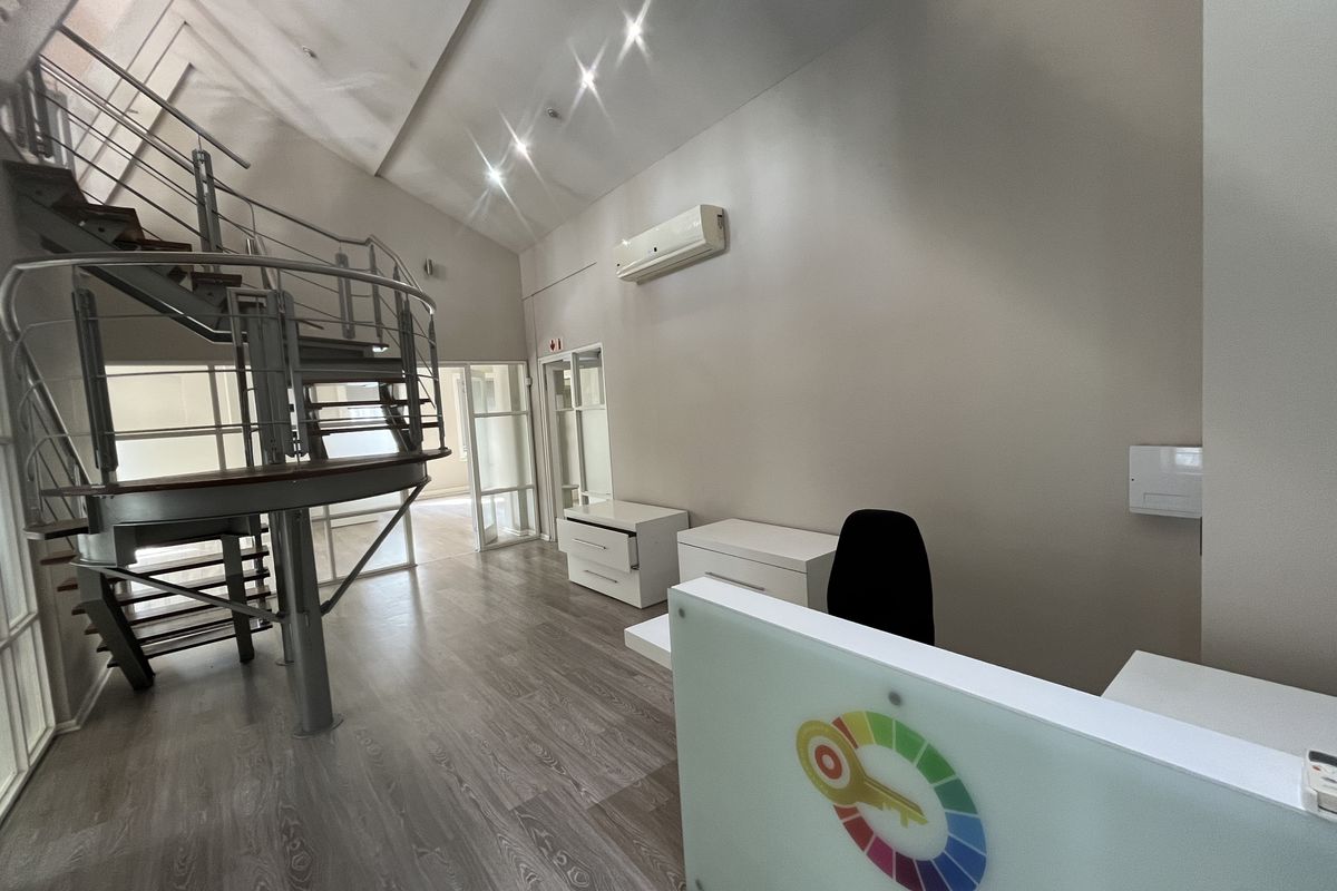 Modern office space featuring a striking spiral staircase, laminate flooring, recessed lighting, and a split-system air conditioner, offering a professional and open work environment.