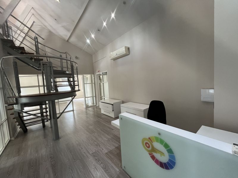 Modern office space featuring a striking spiral staircase, laminate flooring, recessed lighting, and a split-system air conditioner, offering a professional and open work environment.
