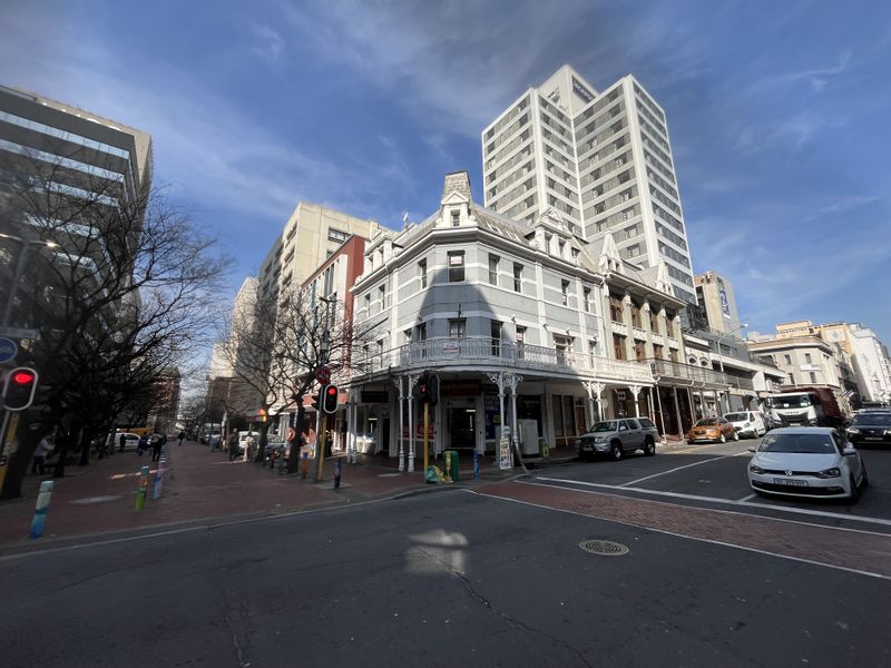 A street-level view of a historic corner office building featuring an ornate wrought iron balcony and classic architectural detailing in a busy urban setting.