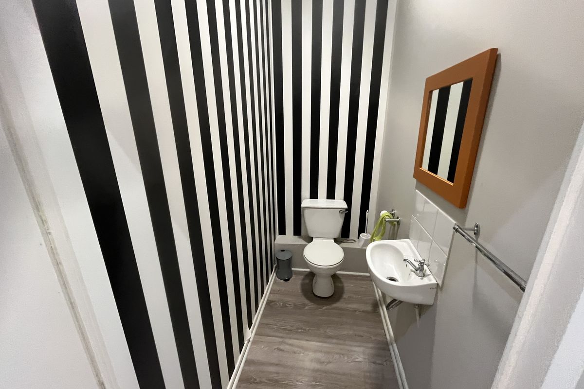 A compact powder room featuring a wall-mounted basin, toilet, and modern laminate flooring with a bold striped feature wall.