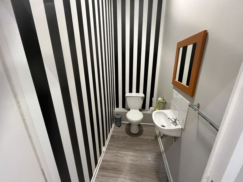 A compact powder room featuring a wall-mounted basin, toilet, and modern laminate flooring with a bold striped feature wall.