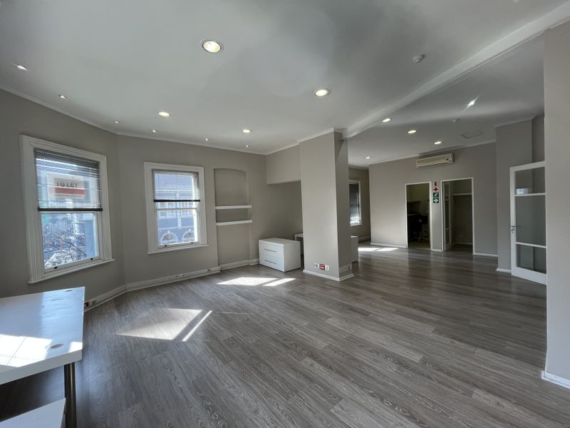 A spacious, well-lit open-plan office area featuring modern laminate flooring, recessed ceiling lights, and an integrated air conditioning unit.