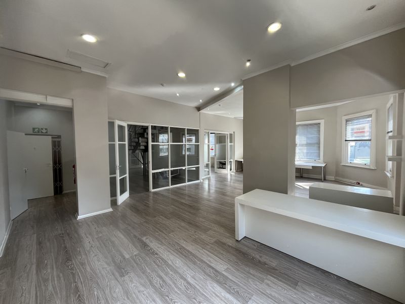Spacious open-plan office area featuring modern laminate flooring, recessed lighting, and glass partition walls, offering a bright and professional workspace environment.