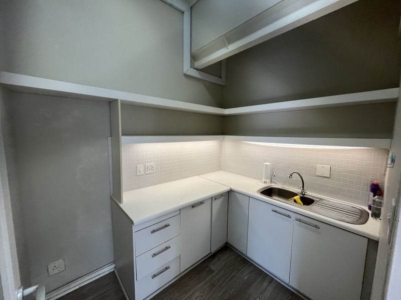 A clean and functional scullery or kitchenette area featuring white built-in cabinetry, a stainless steel sink, tiled backsplash, and integrated under-cabinet lighting.