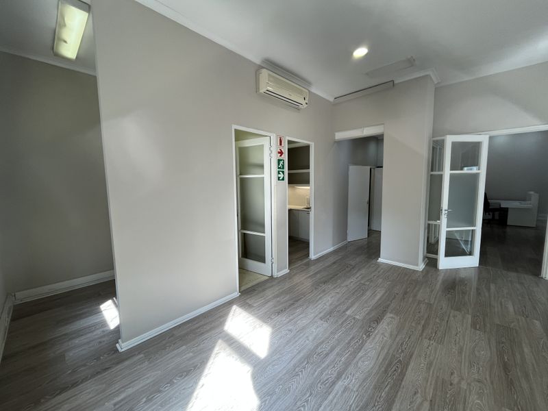 A bright, open-plan office space featuring modern laminate flooring, wall-mounted air conditioning, and multiple access points with frosted glass doors.