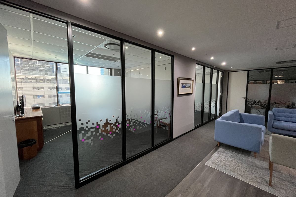 Modern office space featuring glass partition walls with frosted detailing, recessed lighting, and a combination of carpet and vinyl flooring.