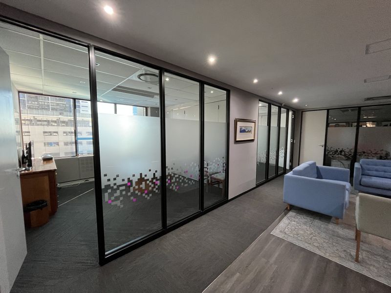 Modern office space featuring glass partition walls with frosted detailing, recessed lighting, and a combination of carpet and vinyl flooring.