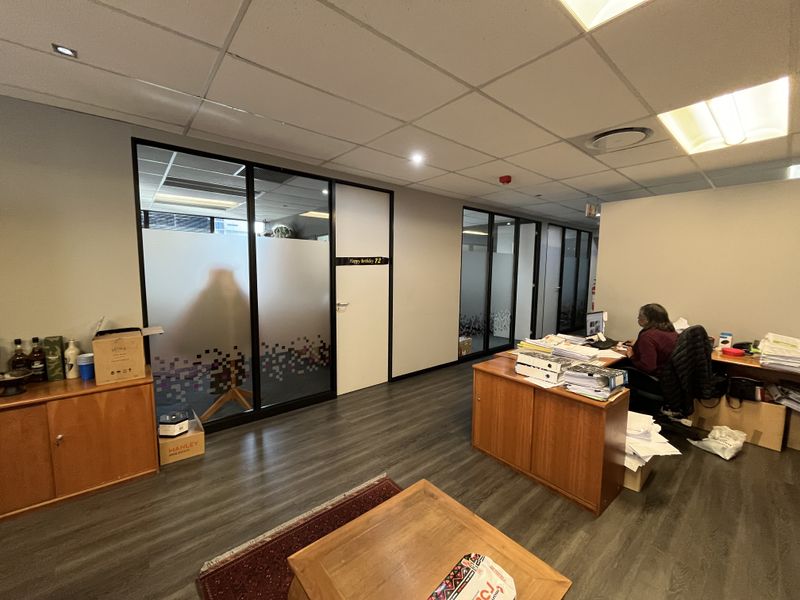 A professional office space featuring glass partition walls, suspended ceilings with recessed lighting, and durable laminate flooring.