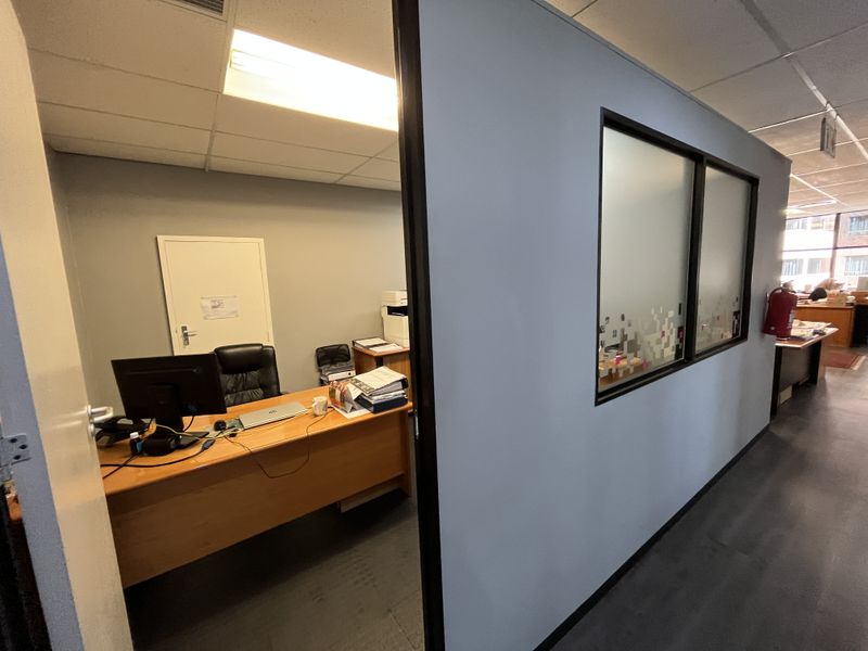 A functional office space featuring a partition wall with frosted glass panels, suspended ceiling, and recessed lighting within a professional commercial environment.