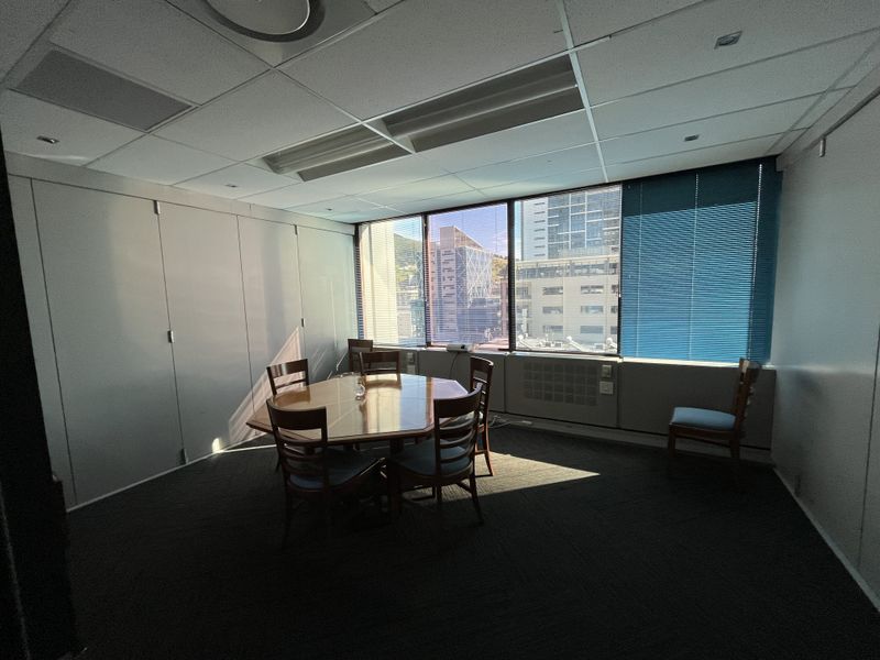 A functional office space featuring a suspended ceiling, large windows with venetian blinds, and integrated HVAC units, offering a professional work environment.