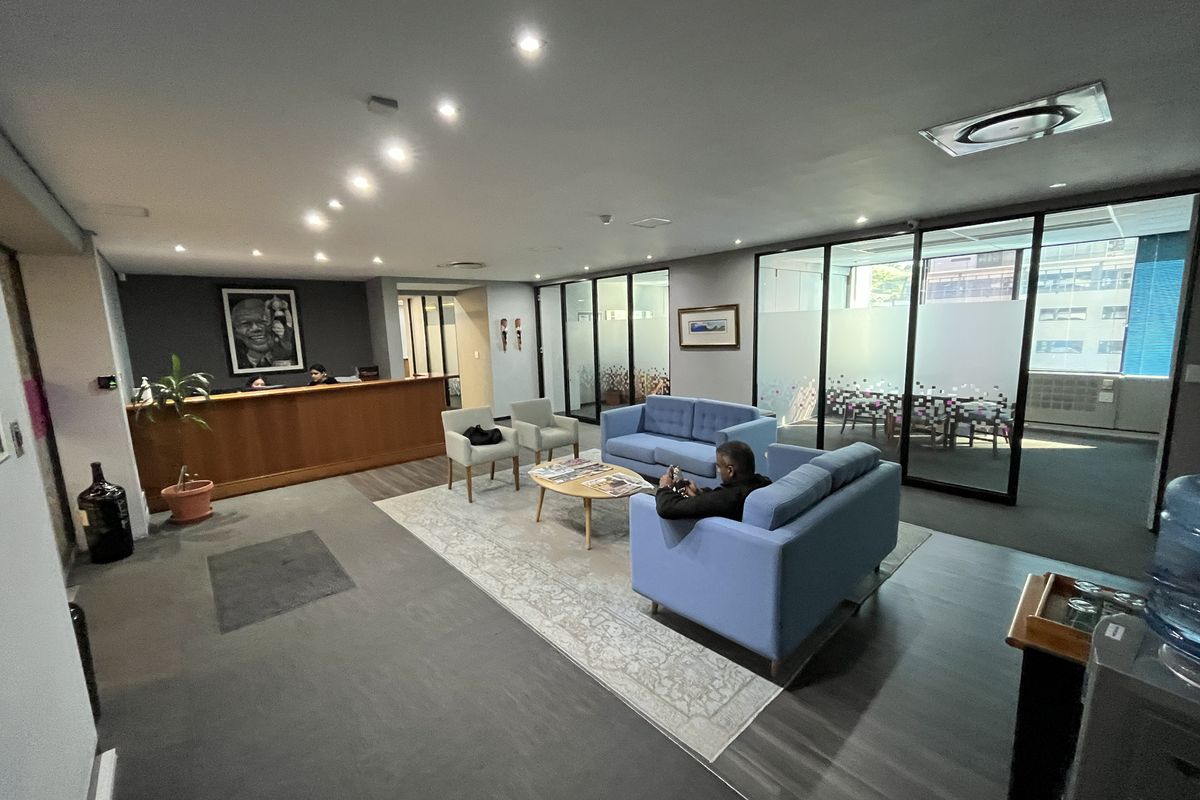 Professional office reception area featuring a built-in wooden desk, glass-partitioned meeting rooms, and modern recessed lighting throughout the space.
