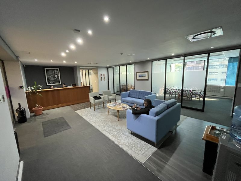 Professional office reception area featuring a built-in wooden desk, glass-partitioned meeting rooms, and modern recessed lighting throughout the space.