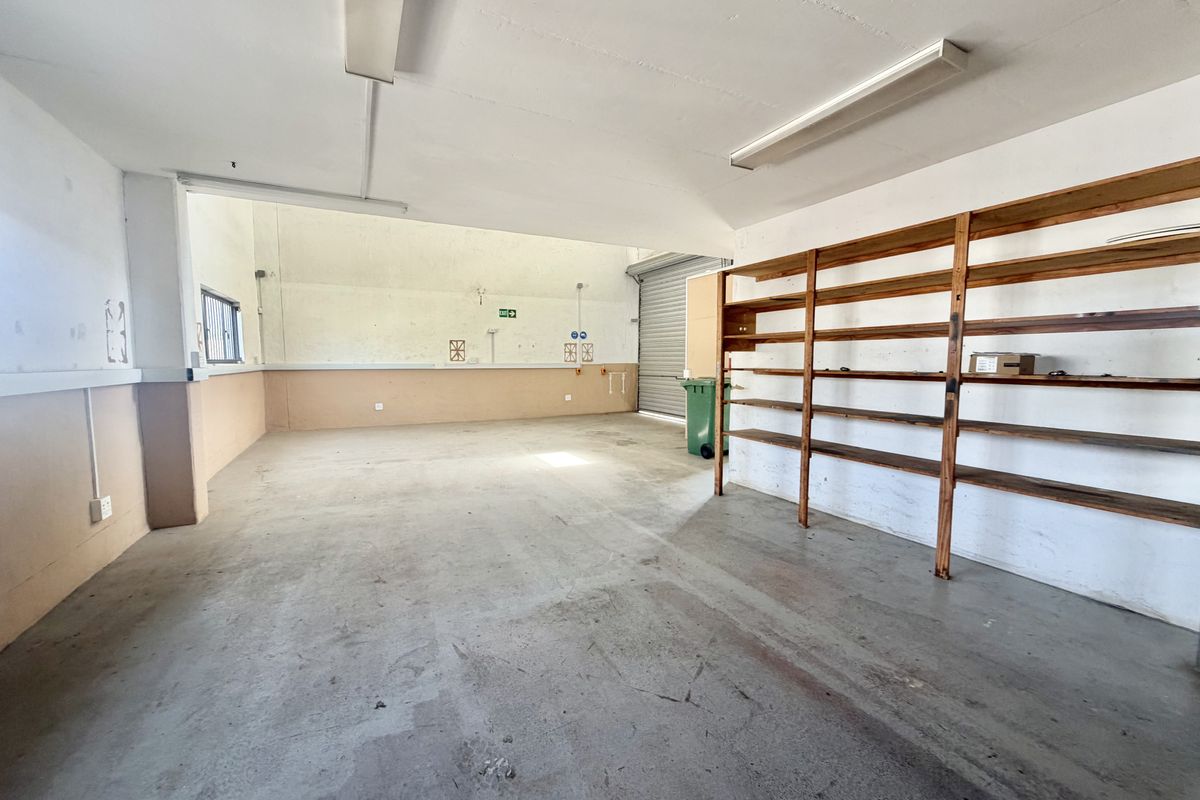 Spacious industrial garage featuring concrete flooring, built-in timber shelving, and a roller shutter door, suitable for storage or workshop use.