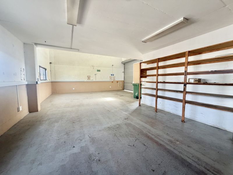 Spacious industrial garage featuring concrete flooring, built-in timber shelving, and a roller shutter door, suitable for storage or workshop use.