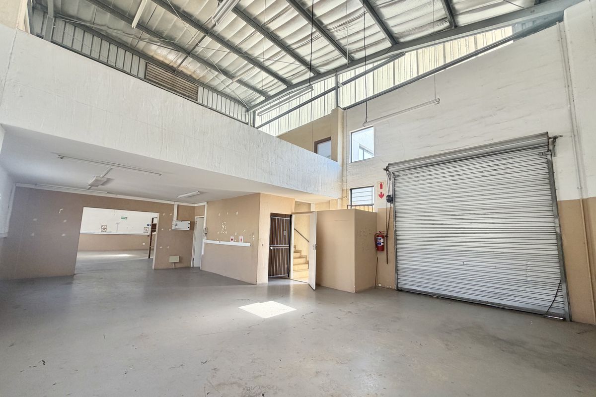 Spacious industrial utility area featuring a high-clearance roller shutter door, exposed steel roof structure, and a mezzanine level, suitable for various commercial operations.