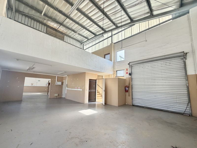 Spacious industrial utility area featuring a high-clearance roller shutter door, exposed steel roof structure, and a mezzanine level, suitable for various commercial operations.