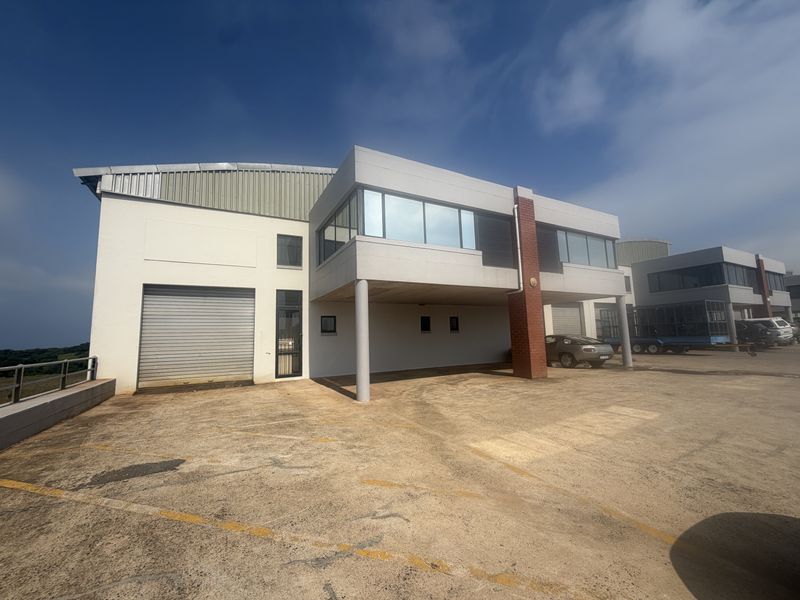 Front exterior view of an industrial property featuring a roller shutter door, concrete columns, and a paved driveway area.