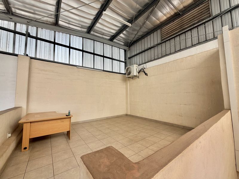 Industrial office space featuring tiled flooring, exposed metal roofing, high-level windows, and a wall-mounted air conditioning unit.