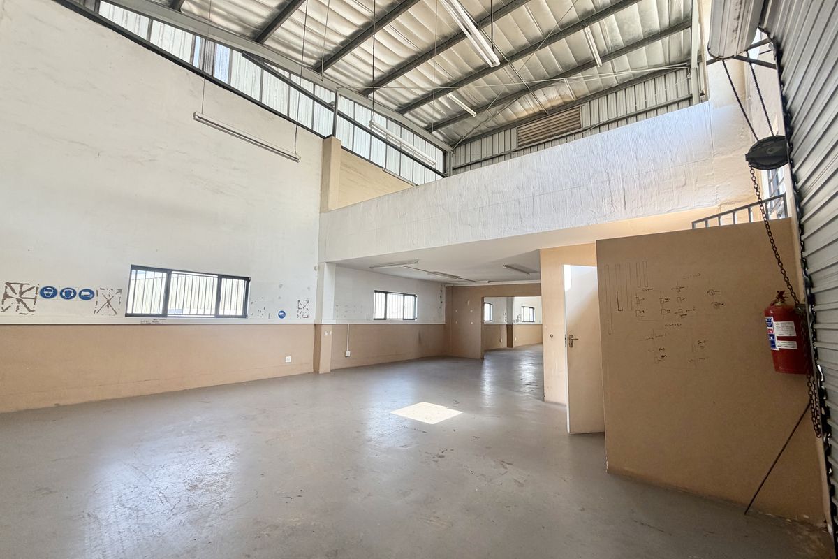 Spacious industrial open-plan unit featuring a mezzanine level, high ceilings with exposed steel trusses, concrete flooring, and ample natural light from clerestory windows.