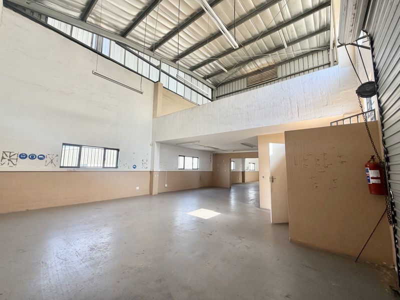Spacious industrial open-plan unit featuring a mezzanine level, high ceilings with exposed steel trusses, concrete flooring, and ample natural light from clerestory windows.