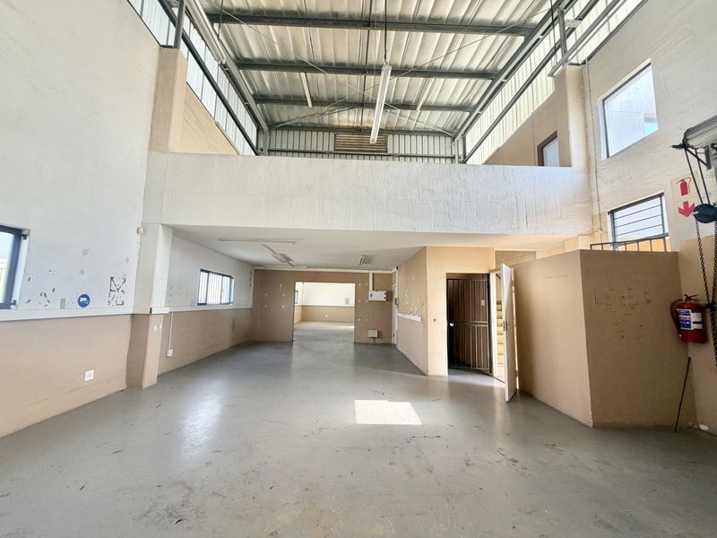 Spacious industrial utility area featuring a mezzanine level, high ceilings with exposed steel structure, and durable concrete flooring, suitable for various commercial or storage uses.