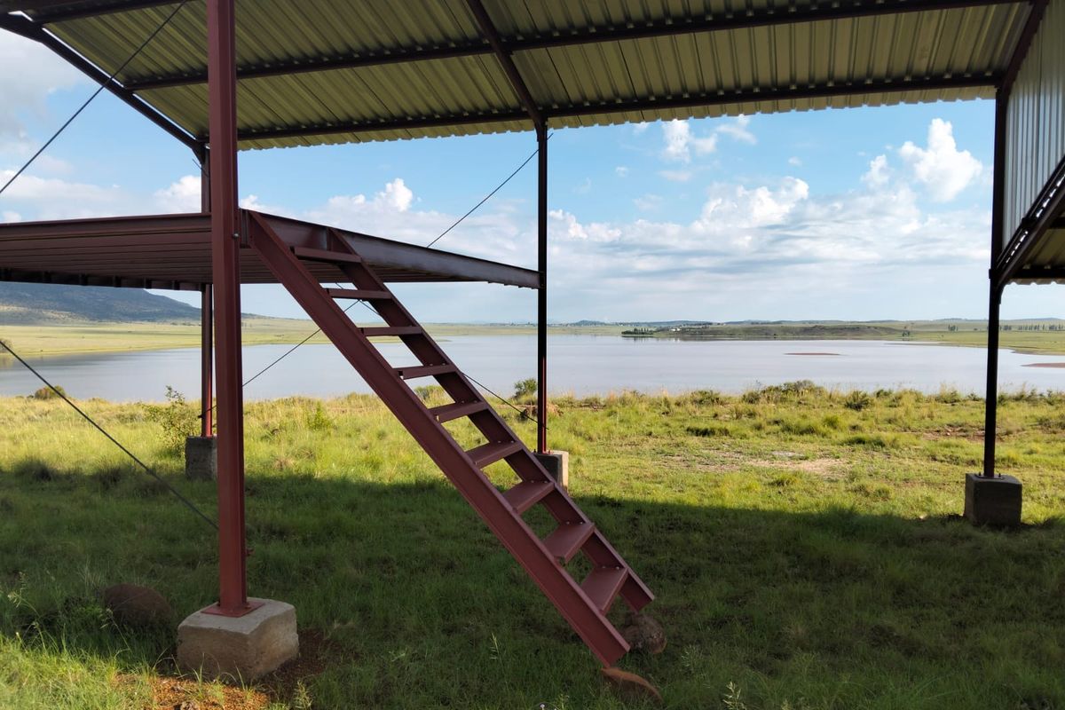 An open-air steel structure with a raised platform and staircase, offering expansive views over the surrounding landscape and water.