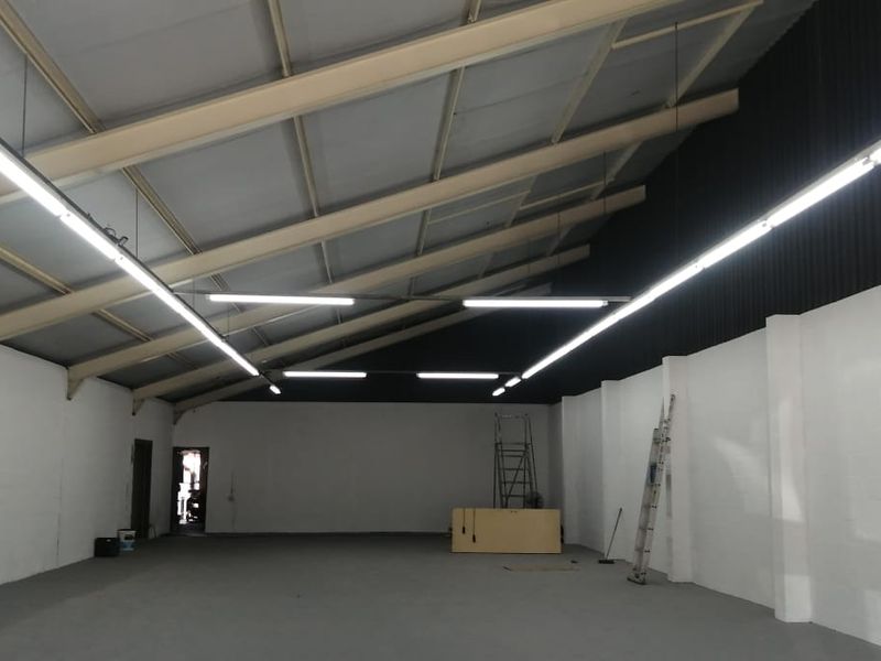 Spacious open-plan retail or utility area featuring high ceilings with exposed steel trusses, fluorescent lighting, and durable concrete flooring.