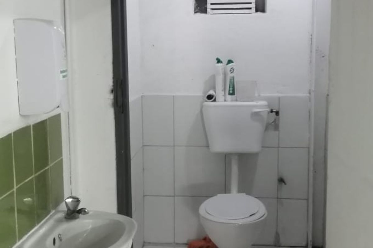 A functional bathroom featuring a wall-mounted basin, toilet, and tiled finishes, requiring some cosmetic updates to improve its overall condition.