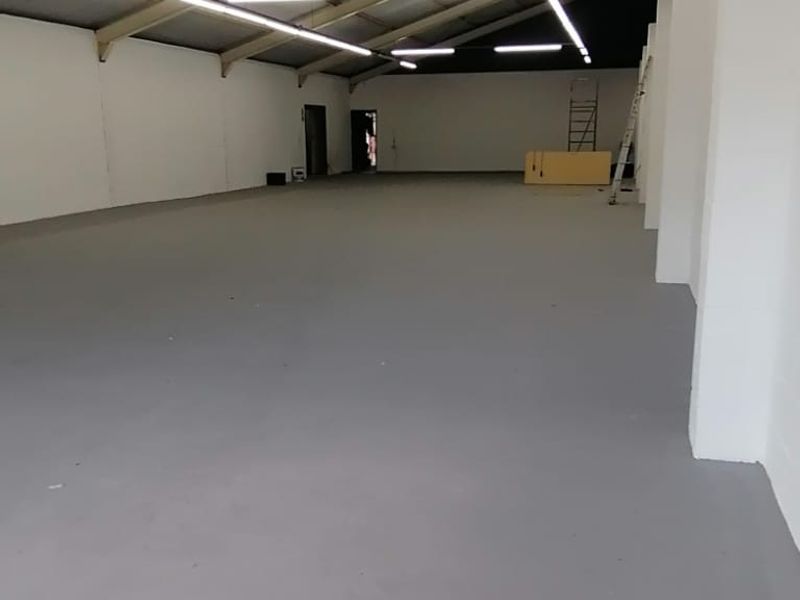 Spacious open-plan retail or industrial unit featuring high ceilings with exposed steel trusses, bright strip lighting, and clean epoxy-coated concrete flooring.