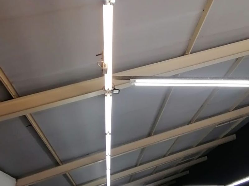 Spacious open-plan retail area featuring exposed steel roof trusses, industrial-style fluorescent lighting, and clean painted concrete flooring, suitable for various commercial uses.