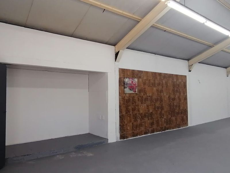 Spacious open-plan retail or utility area featuring high ceilings with exposed steel trusses, fluorescent lighting, and a decorative tiled feature wall.