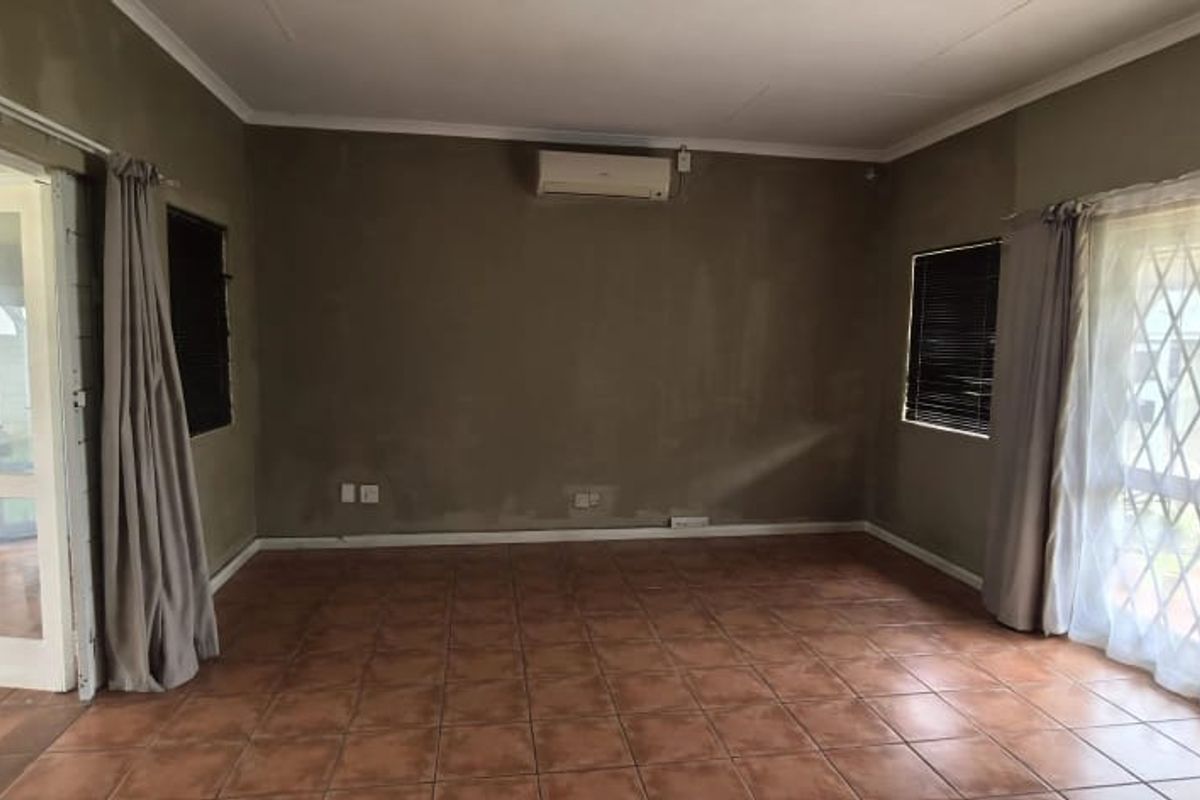 An empty office space featuring tiled flooring, a wall-mounted air conditioning unit, and secure window and door access.