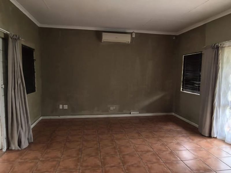 An empty office space featuring tiled flooring, a wall-mounted air conditioning unit, and secure window and door access.