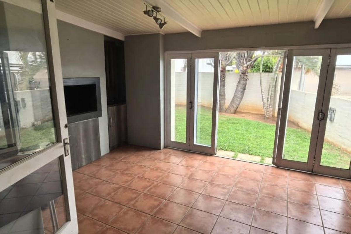 A covered patio area featuring tiled flooring, a built-in braai, and double glass doors opening onto a private garden.