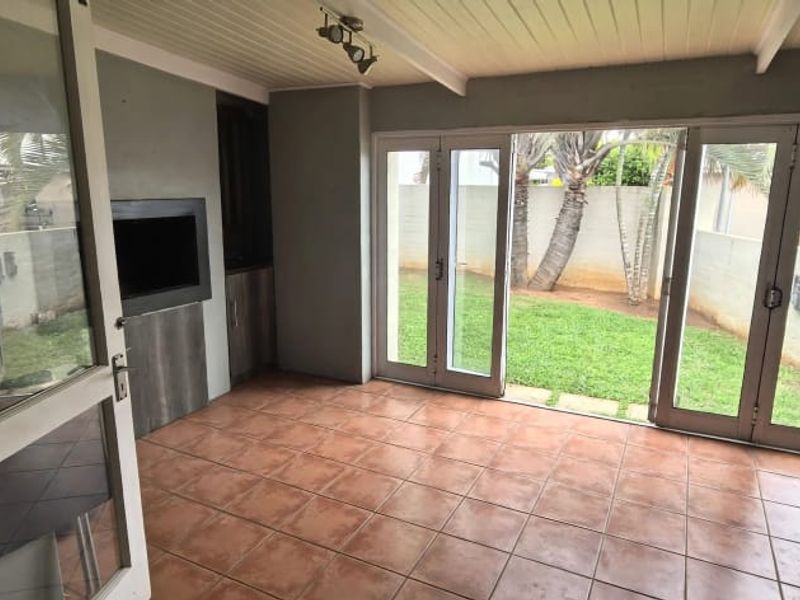 A covered patio area featuring tiled flooring, a built-in braai, and double glass doors opening onto a private garden.