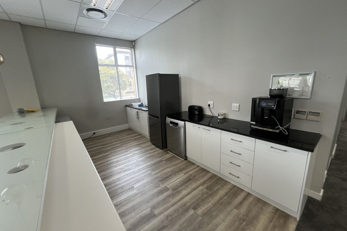 A functional office kitchenette featuring modern white cabinetry, black stone countertops, integrated dishwasher, and durable wood-look laminate flooring.