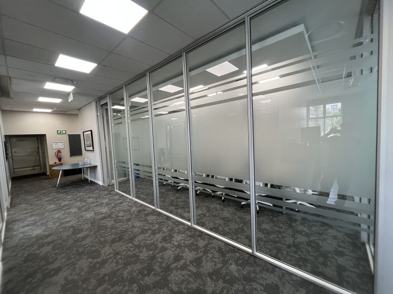 Modern office space featuring a glass partition wall, suspended ceiling with recessed LED lighting, and professional carpeted flooring.