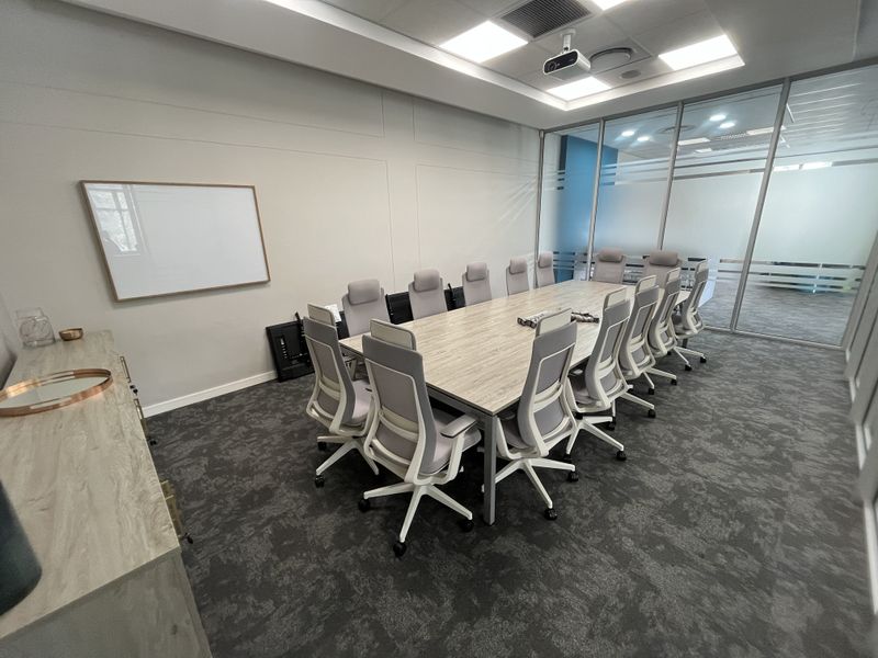 A modern, well-lit office boardroom featuring a large conference table, glass partition walls, and professional ceiling-mounted projector equipment.