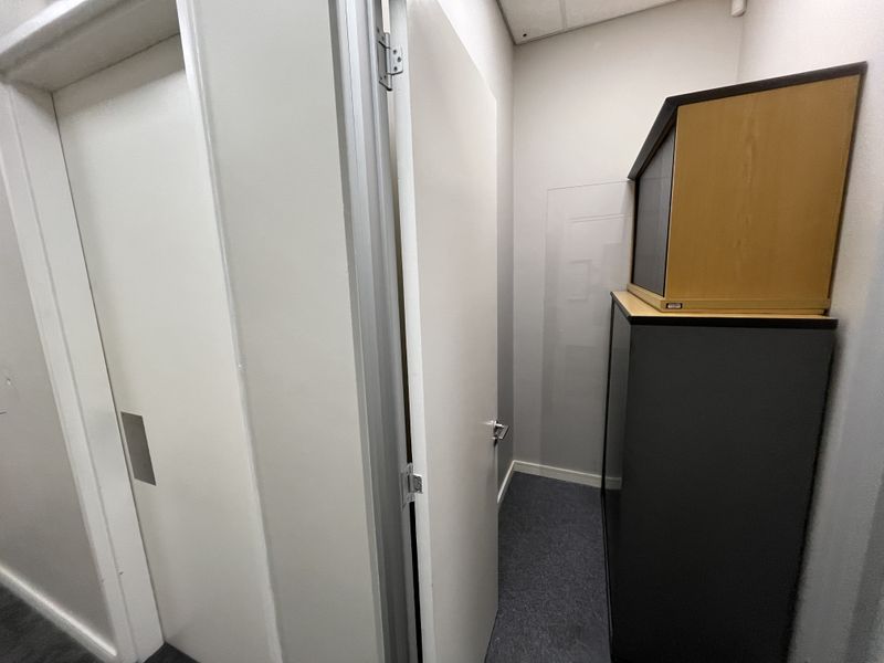 A small utility or storage space featuring carpeted flooring and a suspended ceiling, providing functional storage area within the office premises.