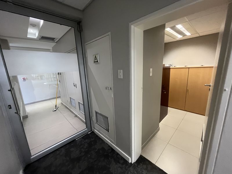 A clean office hallway featuring tiled flooring, a glass partition, and built-in storage cabinetry with recessed ceiling lighting.