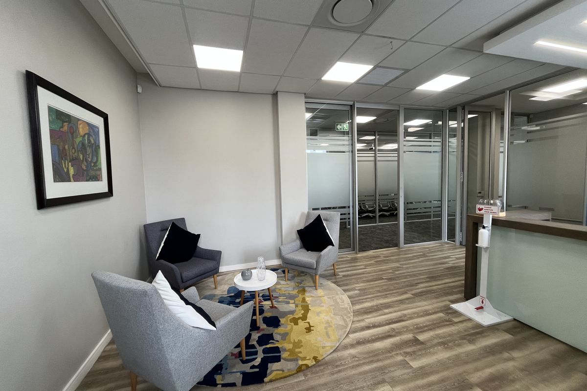 Modern office reception area featuring glass partitions, suspended ceilings with recessed lighting, and durable laminate flooring.