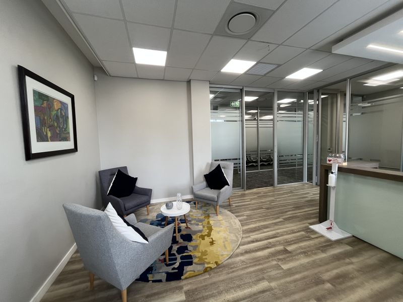 Modern office reception area featuring glass partitions, suspended ceilings with recessed lighting, and durable laminate flooring.