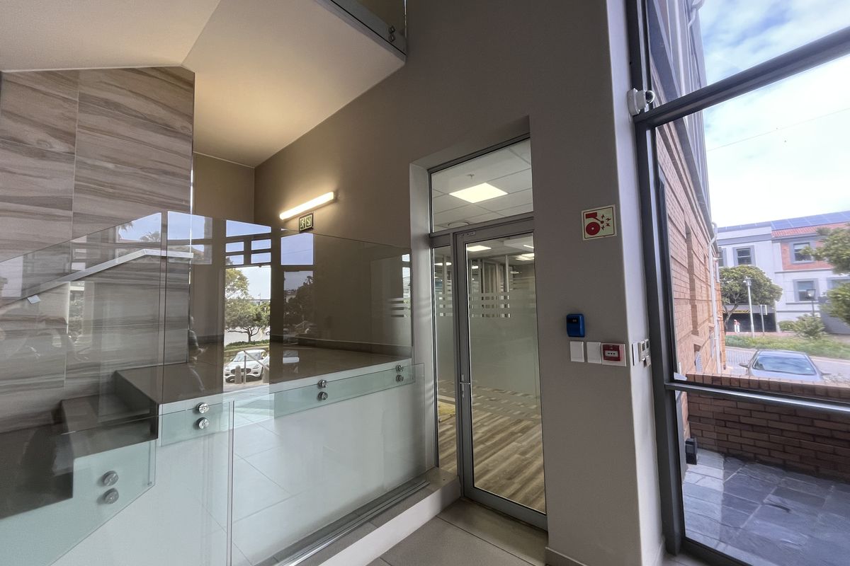Modern office building entrance featuring a glass balustrade staircase, high ceilings, and large windows providing ample natural light and exterior views.