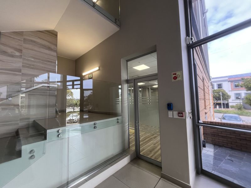 Modern office building entrance featuring a glass balustrade staircase, high ceilings, and large windows providing ample natural light and exterior views.