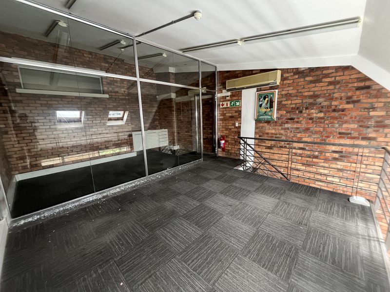 An open-plan office space featuring exposed brick walls, glass partitioning, carpet tile flooring, and a split-system air conditioner.