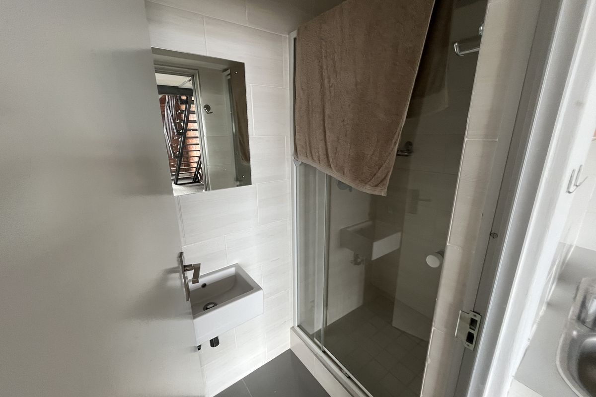Compact office bathroom featuring a wall-mounted basin, tiled finishes, and a glass-enclosed shower unit.