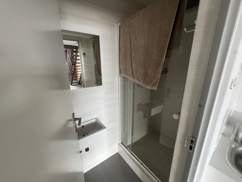 Compact office bathroom featuring a wall-mounted basin, tiled finishes, and a glass-enclosed shower unit.