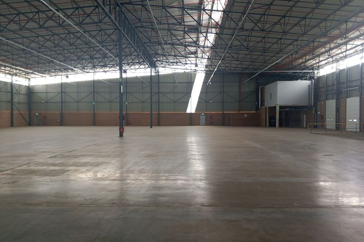 Spacious industrial warehouse featuring high exposed steel roof trusses, polished concrete flooring, and integrated mezzanine office space with roller shutter access.