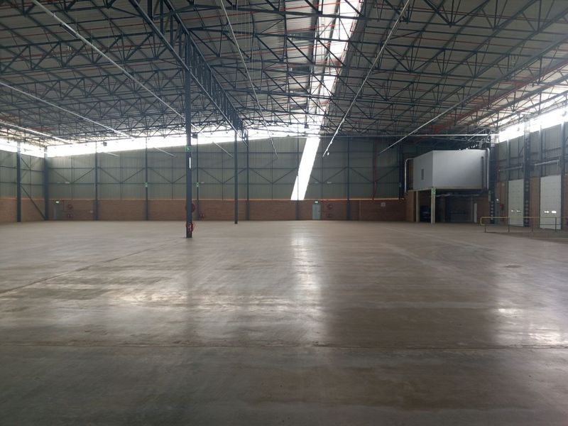Spacious industrial warehouse featuring high exposed steel roof trusses, polished concrete flooring, and integrated mezzanine office space with roller shutter access.