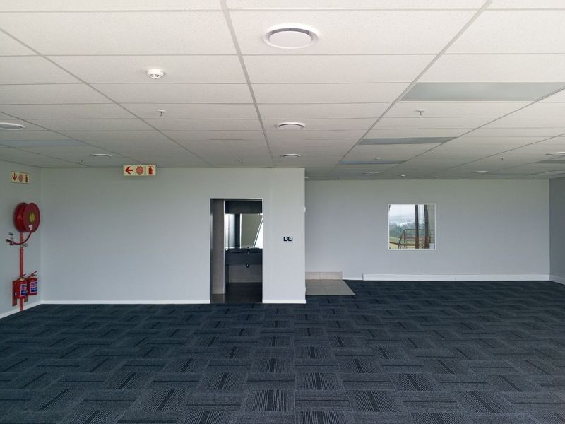 Spacious open-plan industrial office area featuring suspended ceilings, recessed lighting, carpet tiles, and integrated fire safety equipment.